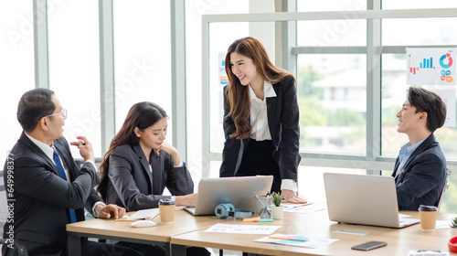 Asian professional successful businesswoman manager entrepreneur in formal suit standing teaching brainstorming marketing strategy with male female businessmen employees team in company meeting room