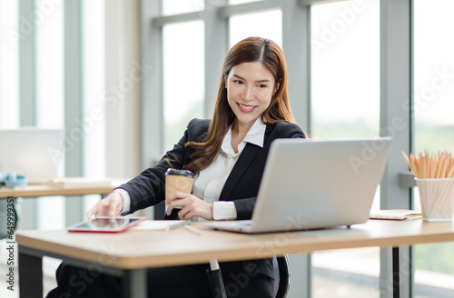 Portrait shot of Asian professional successful female businesswoman secretary employee in formal suit sitting smiling look at camera taking break drink coffee browsing tablet online in company office