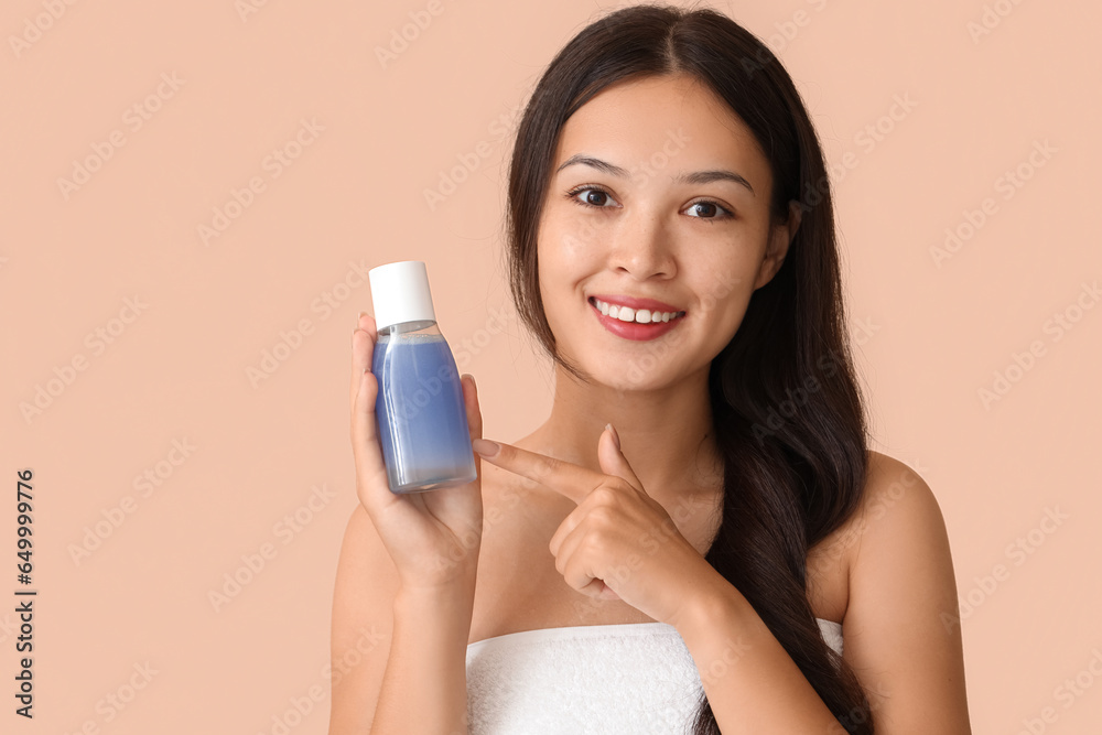 Young Asian woman pointing at bottle of micellar water on beige background, closeup Young Asian woman pointing at bottle of micellar water on beige background, closeup