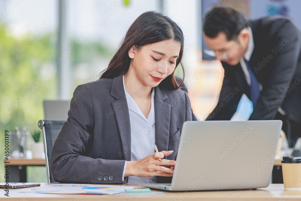 Portrait shot of Asian professional successful female businesswoman secretary employee in formal suit sitting smiling look at camera typing laptop notebook computer at working desk in company office Portrait shot of Asian professional successful female businesswoman secretary employee in formal suit sitting smiling look at camera typing laptop notebook computer at working desk in company office
