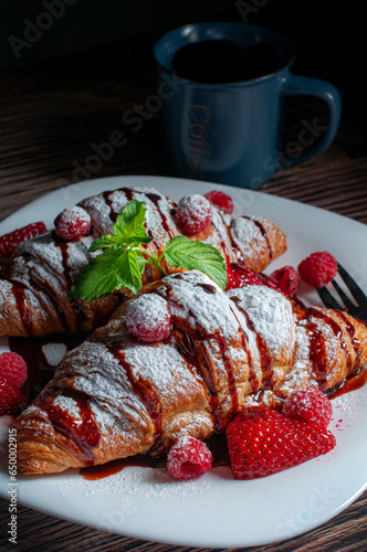  Macro photography croissant or crossaints on a white plate with strawberries, raspberries, and sugar glass or candy glass with chocolate syrup on top 