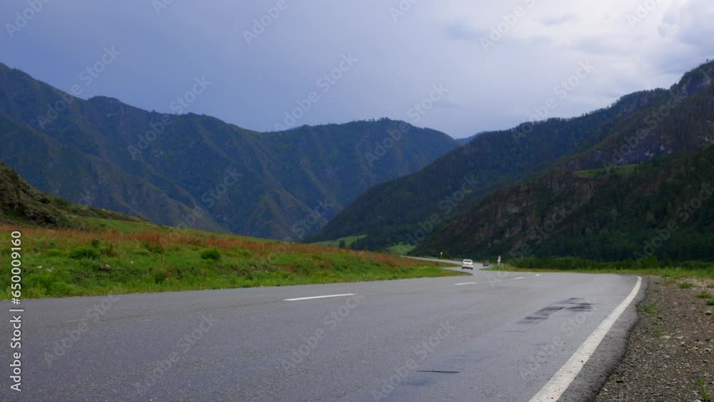 White passenger car drove slowly into the mountains on a smooth asphalt road. The journey by car takes you through a breathtaking landscape of mountains, plains and valleys
