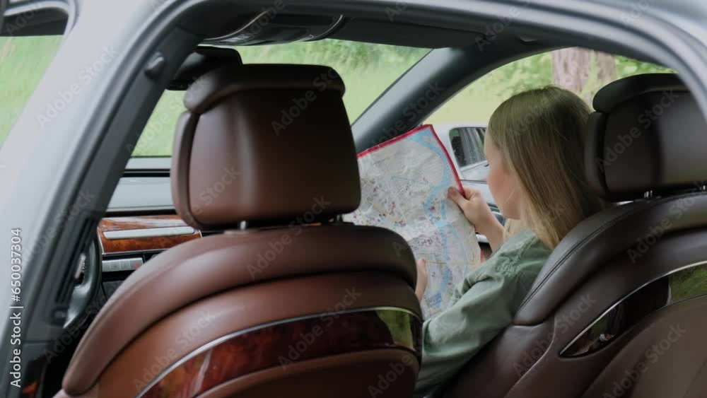 Smiling young woman sitting in car on road check the route on travel map. Slow motion Local solo travel on weekends concept. Exited woman explore freedom outdoors in forest. Unity with nature Smiling young woman sitting in car on road check the route on travel map. Slow motion Local solo travel on weekends concept. Exited woman explore freedom outdoors in forest. Unity with nature