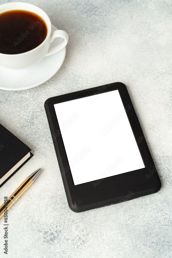Composition with modern e-book reader, hardcover book and cup of coffee on table Composition with modern e-book reader, hardcover book and cup of coffee on table