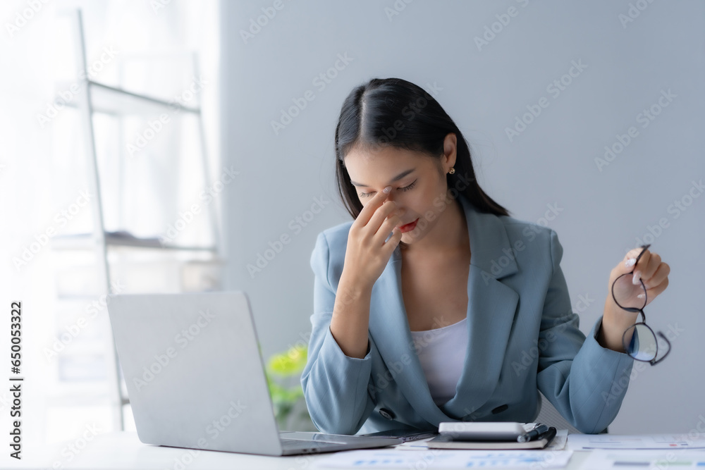 Young Asian woman feeling migraine head strain. Tired, Overworked businesswoman financier while working on laptop computer in office. Young Asian woman feeling migraine head strain. Tired, Overworked businesswoman financier while working on laptop computer in office.