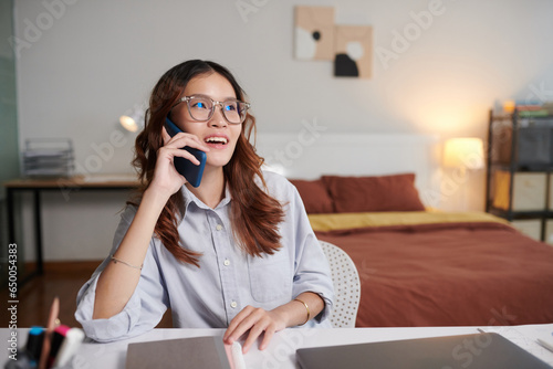 Portrait of young businesswoman sitting at desk in bedroom and calling on phone photo