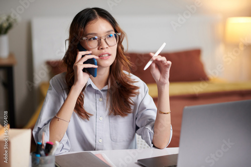 Young woman spinning pen when talking on phone with friend or coworker photo