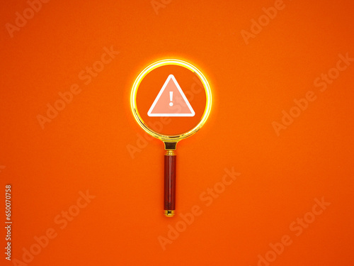 Exclamation mark and warning text on a magnifying glass over an orange background.