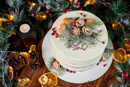 Christmas cake made of chocolate base with cream, decorated with spruce branches, walnuts and pomegranate seeds against the backdrop of Christmas decor