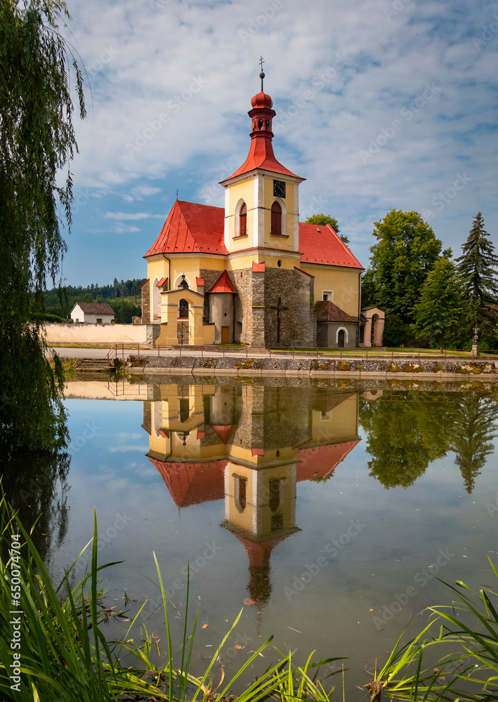 A church on the bank of a pond illuminated by the sun at sunset in the village of Mlade Briste, Czech A church on the bank of a pond illuminated by the sun at sunset in the village of Mlade Briste, Czech