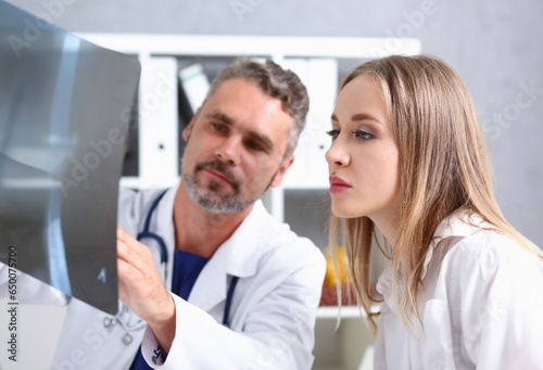 Mature male doctor hold in arm and look at xray photography discussing it with female patient portrait. Bone disease exam medic assistance cancer test healthy lifestyle hospital practice concept photo