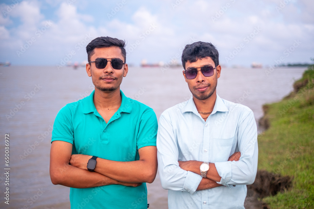 South asian young handsome boys in front of a river, portrait of young friends , sunglasses on their eyes 