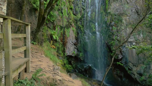 Observation Deck With Aguacaida Waterfall Flowing Down On Mossy Cliff Within The Forest. - aerial tilt up photo