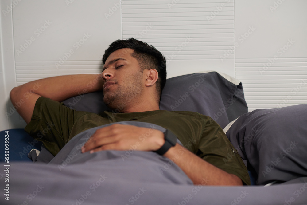 Young man with smartwatch sleeping in bed