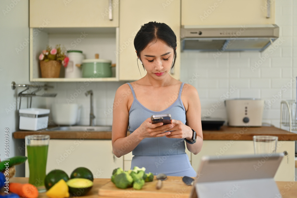 Sporty young woman using smartphone in kitchen, checking social media or searching for new recipe Sporty young woman using smartphone in kitchen, checking social media or searching for new recipe