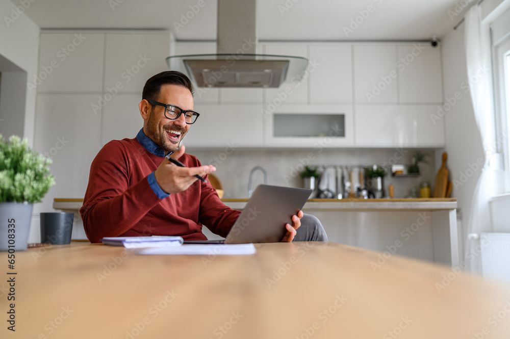 Happy male freelancer discussing over video call on laptop while sitting at desk in home office Happy male freelancer discussing over video call on laptop while sitting at desk in home office