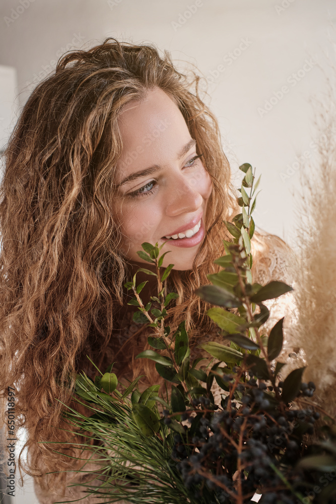 Naklejka premium Positive blond lady near green plants in studio