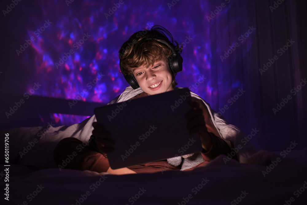 Positive boy in headphones watching video on tablet in darkness Positive boy in headphones watching video on tablet in darkness