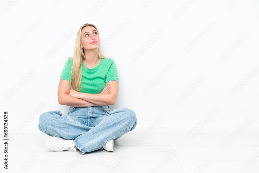 Young caucasian woman sitting on the floor isolated on white background looking up while smiling Young caucasian woman sitting on the floor isolated on white background looking up while smiling