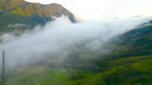 Morning in Oxapampa, Peru, captured from a high-angle drone perspective. A slow, cinematic rotation around the clouds reveals the cloud-covered village, with houses, forested lands, and hills in view. photo