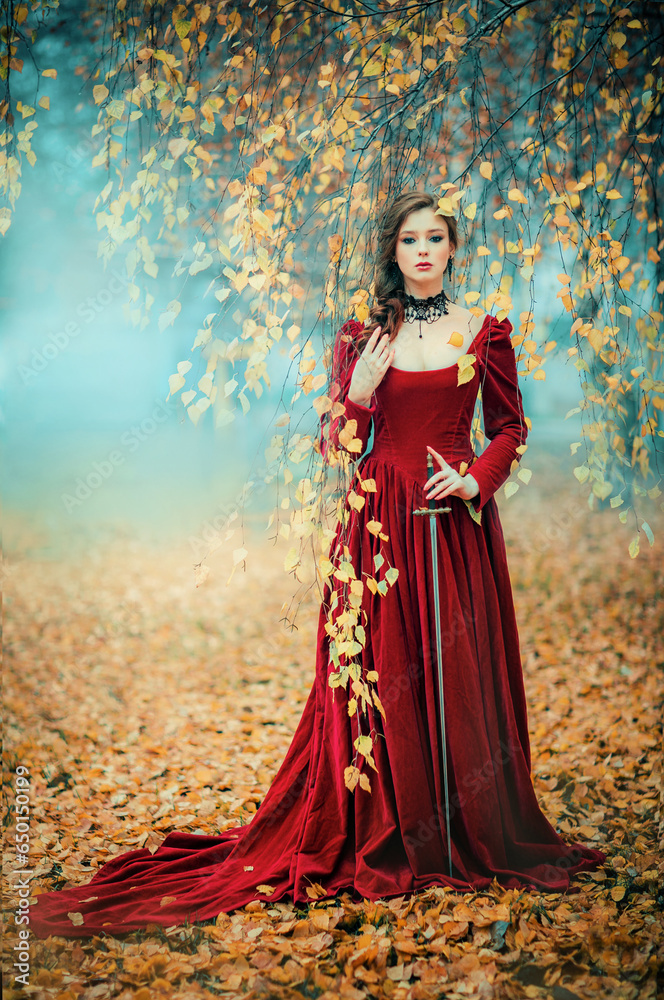 Portrait of magnificent Fashion gothic girl standing in autumn forest .Fantasy art work.Amazing red haired model in claret dress with a sword .Fairytale about young princess-warrior. Portrait of magnificent Fashion gothic girl standing in autumn forest .Fantasy art work.Amazing red haired model in claret dress with a sword .Fairytale about young princess-warrior.