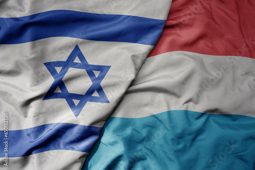 big waving national colorful flag of israel and national flag of luxembourg .