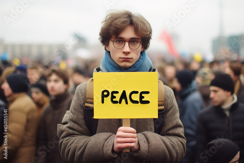 Young man holding peace banner during protest against war and aggression with hundreds people in the background. © Bojan