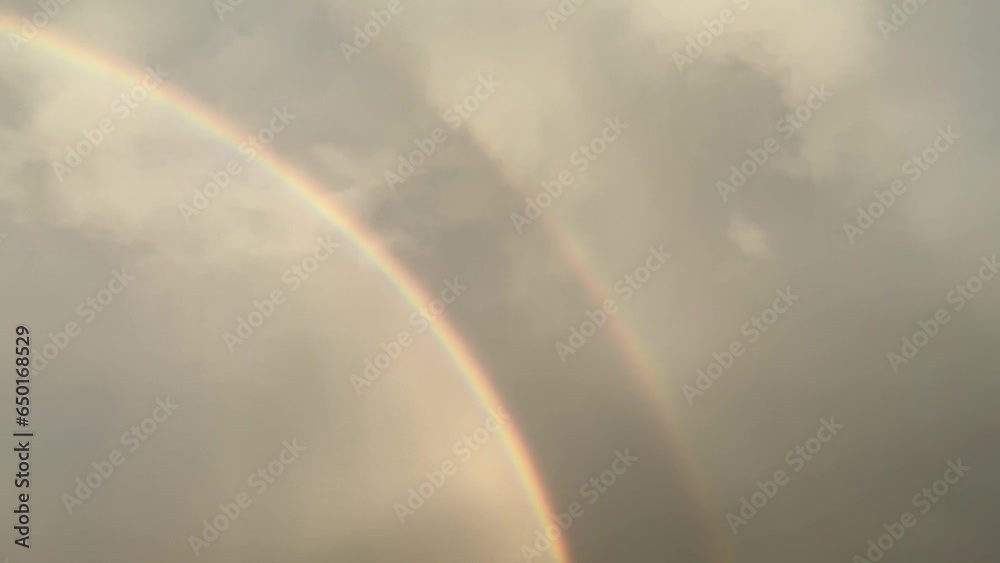 Brightened sky by sunlight with colorful rainbows and gray rainy clouds during rainfall - slow motion. Topics: weather, meteorology, optical phenomenon, natural colors Brightened sky by sunlight with colorful rainbows and gray rainy clouds during rainfall - slow motion. Topics: weather, meteorology, optical phenomenon, natural colors