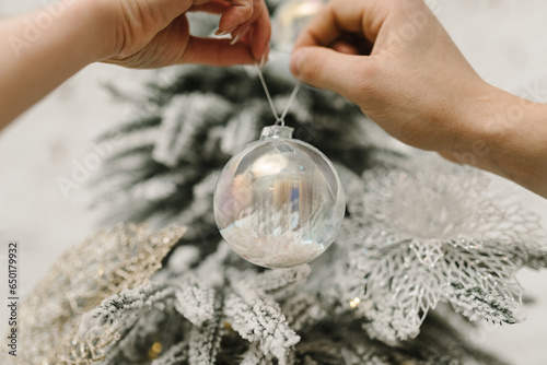 A couple decorating a Christmas tree with a toy ball. Merry Christmas and Happy Holidays. Hands man and woman decorate tree indoors. The morning before Xmas. Decorated interior of a house. Closeup.