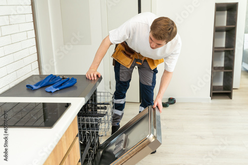 Full length of repairman repairing dishwasher with screwdriver in kitchen.
