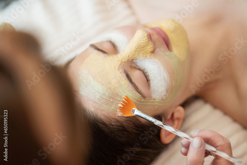 Female cosmetologist applying masks of different types on the face of young girl client. Using modern cosmetics for cleansing, moisturizing, brightening, exfoliating and tightening the skin photo