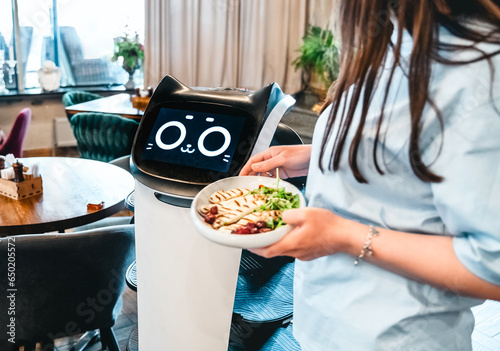 Robot waiter serve food at modern restaurant table.Offering innovation futuristic high-tech automated dining experience.Bringing,delivery automation order to customer.Digital robotic AI smart service