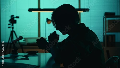 Medium silhouette video of a suspect, offender, perpetrator or prisoner sitting in the interrogation room. He is studying the evidence on the table. photo
