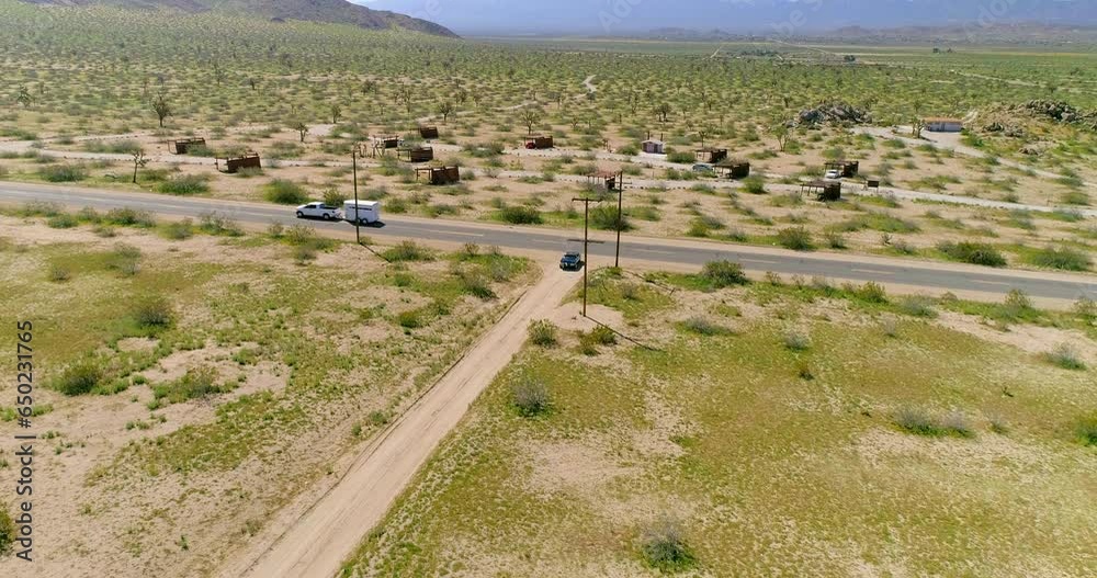 Aerial Lockdown Shot Of Vehicles On Road Amidst Plants Near Mountains On Sunny Day - Joshua Tree, California