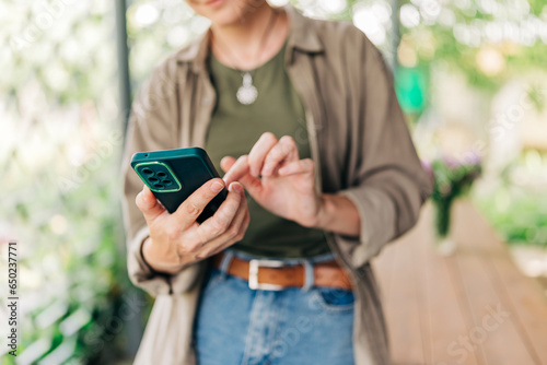 Woman hands close-up holding mobile phone device in the yard house terrace