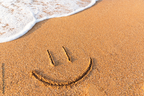 Fototapeta Naklejka Na Ścianę i Meble -  smile painted on the sand next to a foamy wave. Sandy beach with a friendly message written on it