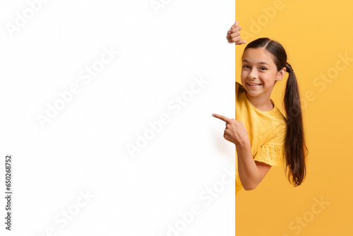 Positive adorable girl teenager pointing at empty advertising board