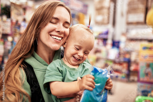 Young attractive mother with cute baby in her hands walking around toy store. Beautiful mom and her little blonde daughter are shopping in the mall and having fun. Family weekend, happy childhood.