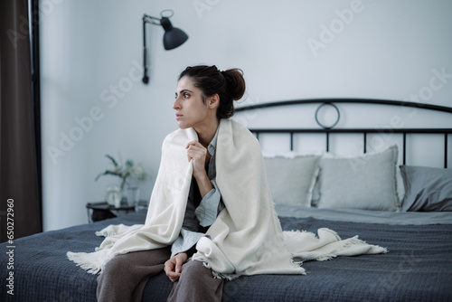 Frustrated brunette woman in blanket suffering from emotional pain on bed at home