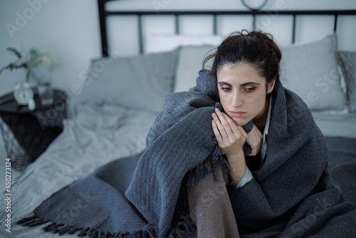 Distressed brunette woman in blanket looking away while sitting on bed at home, emotional pain concept
