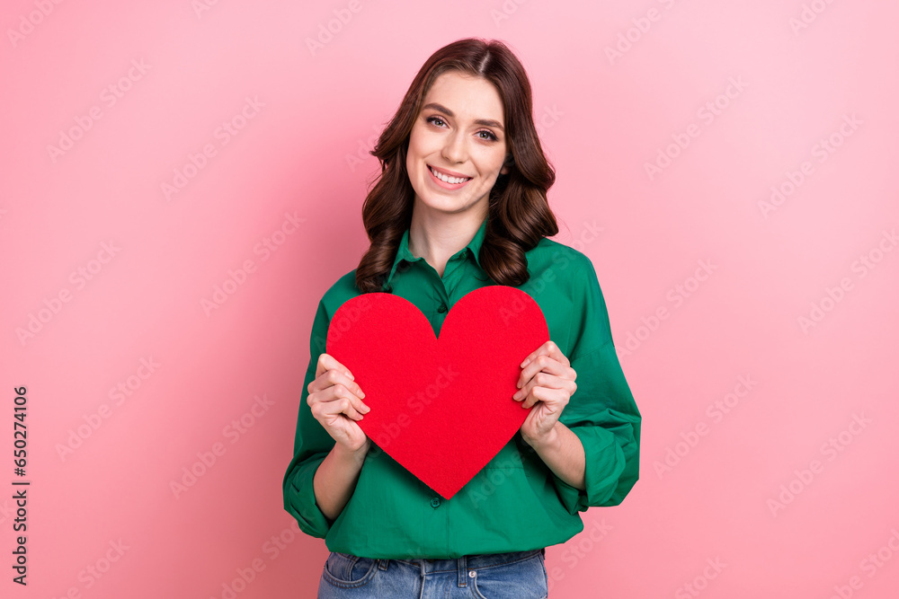 Photo of cheerful positive woman dressed green shirt holding red paper heart isolated pink color background Photo of cheerful positive woman dressed green shirt holding red paper heart isolated pink color background