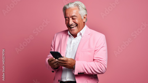 An elderly man smiling and laughing with his phone against a colored background. photo