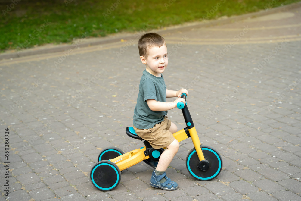 A cute toddler boy of two or three years old rides a bicycle or balance bike in a city park on a sunny summer day. Toddlerhood and childhood concept. Selective focus A cute toddler boy of two or three years old rides a bicycle or balance bike in a city park on a sunny summer day. Toddlerhood and childhood concept. Selective focus