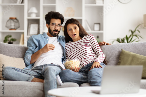 Shocked eastern couple watching TV together at home photo