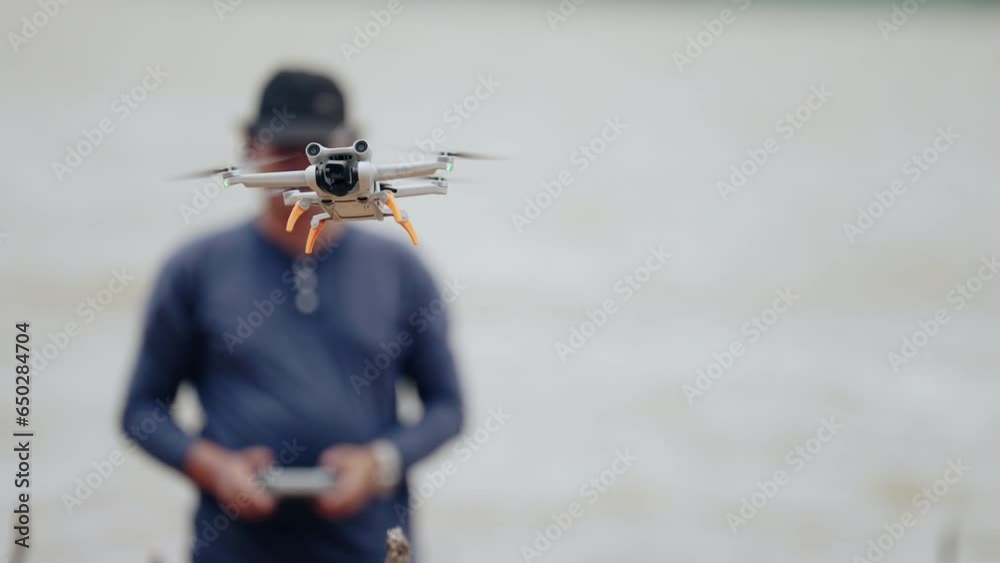 Man controls the drone using sticks on the remote control landing drone in his hands after recording video and flying in natural scenic place.