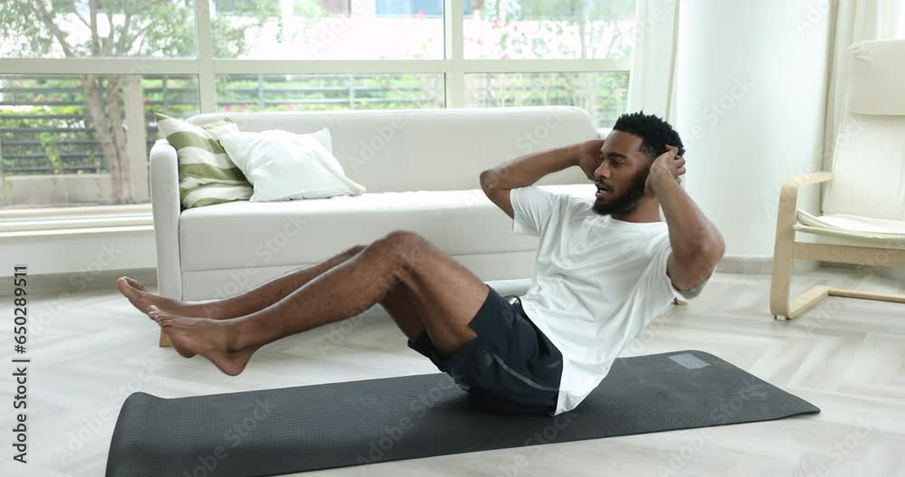 Millennial muscular African man in activewear doing abdominals sit up training on mat in living room, crisscross exercise for abs relief. Fitness, work out at home, healthy active lifestyle routine Millennial muscular African man in activewear doing abdominals sit up training on mat in living room, crisscross exercise for abs relief. Fitness, work out at home, healthy active lifestyle routine
