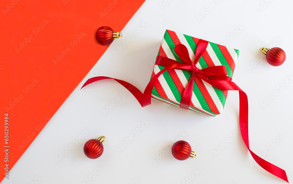 Obraz premium Christmas gift wrapped in striped paper on the white and red background. Top view. Copy space.