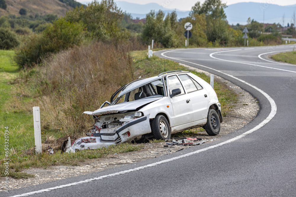 White car wrecked on the side of the road, abandoned after a head-on collision accident