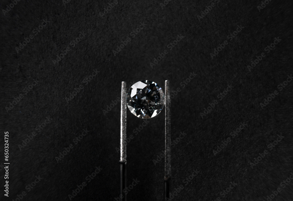 Obraz premium macro view from above of a diamond gripped with tweezers on black background