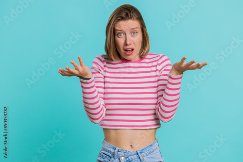 What Why. Sincere irritated young woman raising hands in indignant expression, ask reason of failure demonstrating disbelief irritation by trouble. Pretty confused girl in crop top on blue background photo